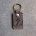 Country gray leather keychain debossed with a coyote track above the words Fresh snow FRESH TRACKS, on gray plaster