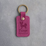 Fuchsia pink leather keychain debossed with a Papillon silhouette and the words Fringe BENEFITS, on gray concrete