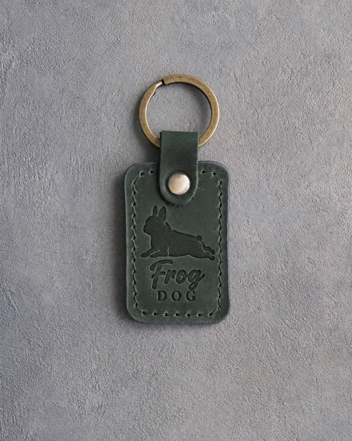 Forest green leather keychain debossed with a French bulldog silhouette and the words Frog DOG, on gray concrete