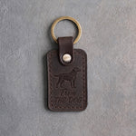 Dark espresso leather keychain debossed with a Labrador retriever silhouette above From and THE DOG, on gray concrete