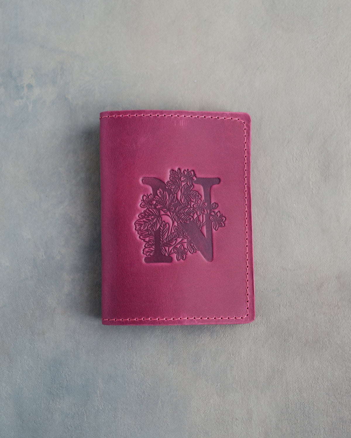 Fuchsia leather passport cover with a large floral initial N pressed into the front