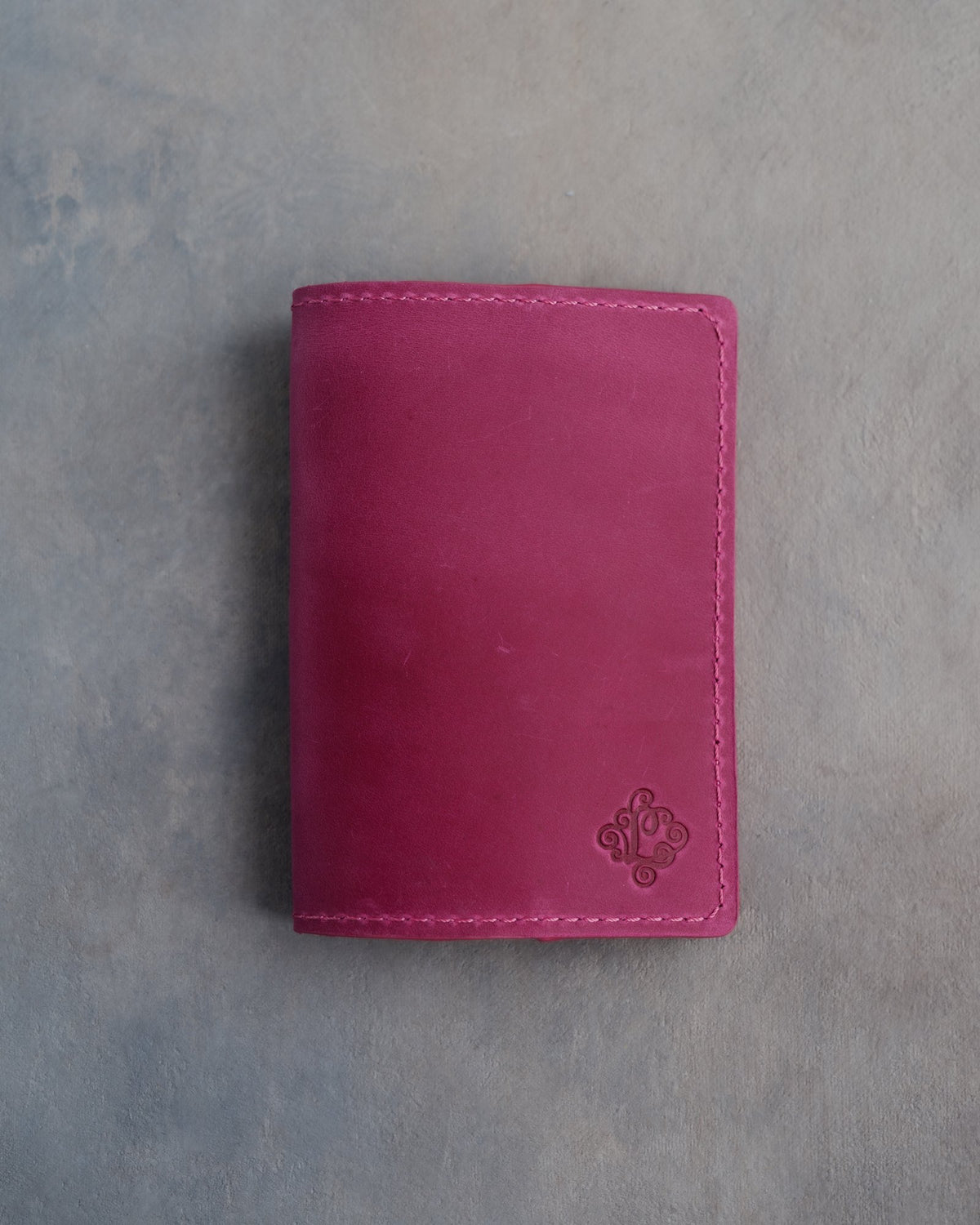 Fuchsia leather passport cover with a flower initial pressed into the bottom corner