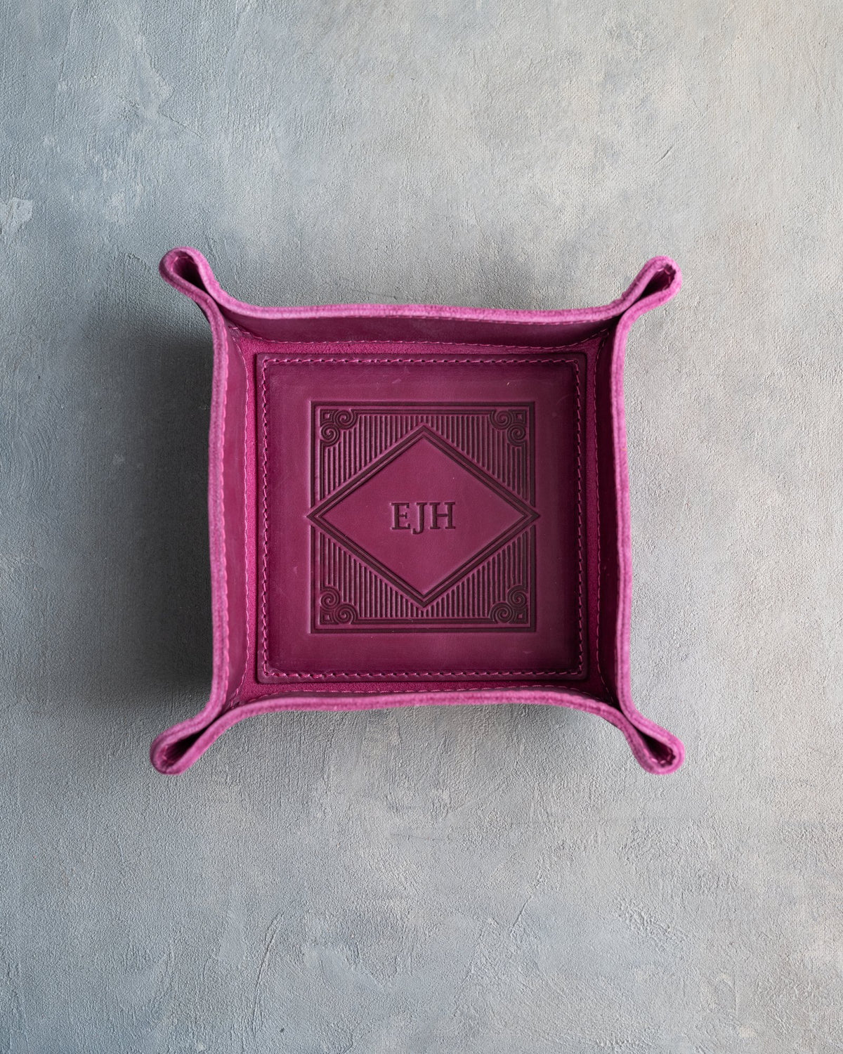 Fuchsia leather valet tray with snapped corners and the initials EJH pressed into the diamond frame, seen from above