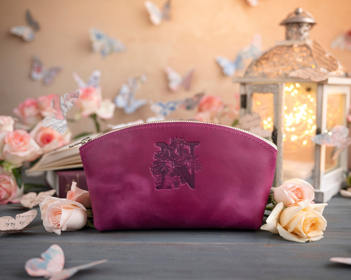 Fuchsia leather makeup bag stamped with a floral initial N, surrounded by blush roses
