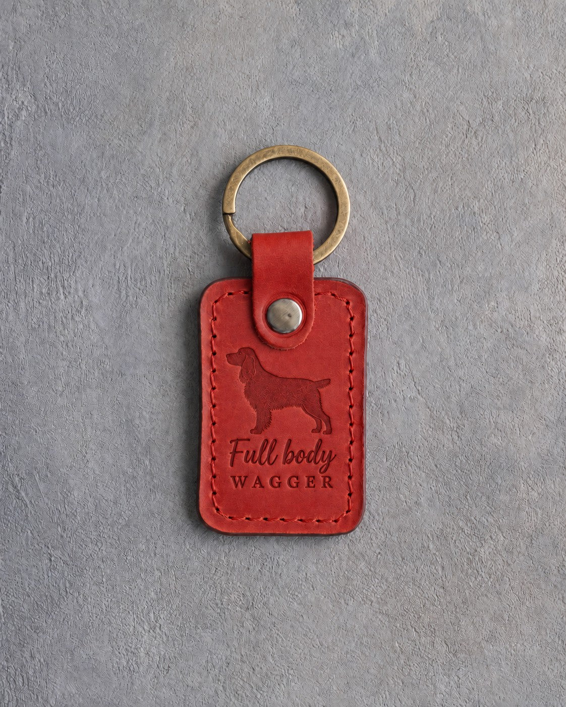 Poppy red leather keychain debossed with a springer spaniel and the words Full body WAGGER, on gray concrete