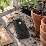 Black Fun Guy keychain on a mossy log beside a cluster of wild mushrooms in the woods
