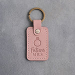 Blush pink leather keychain debossed with a solitaire engagement ring above the words Future MRS, on gray concrete