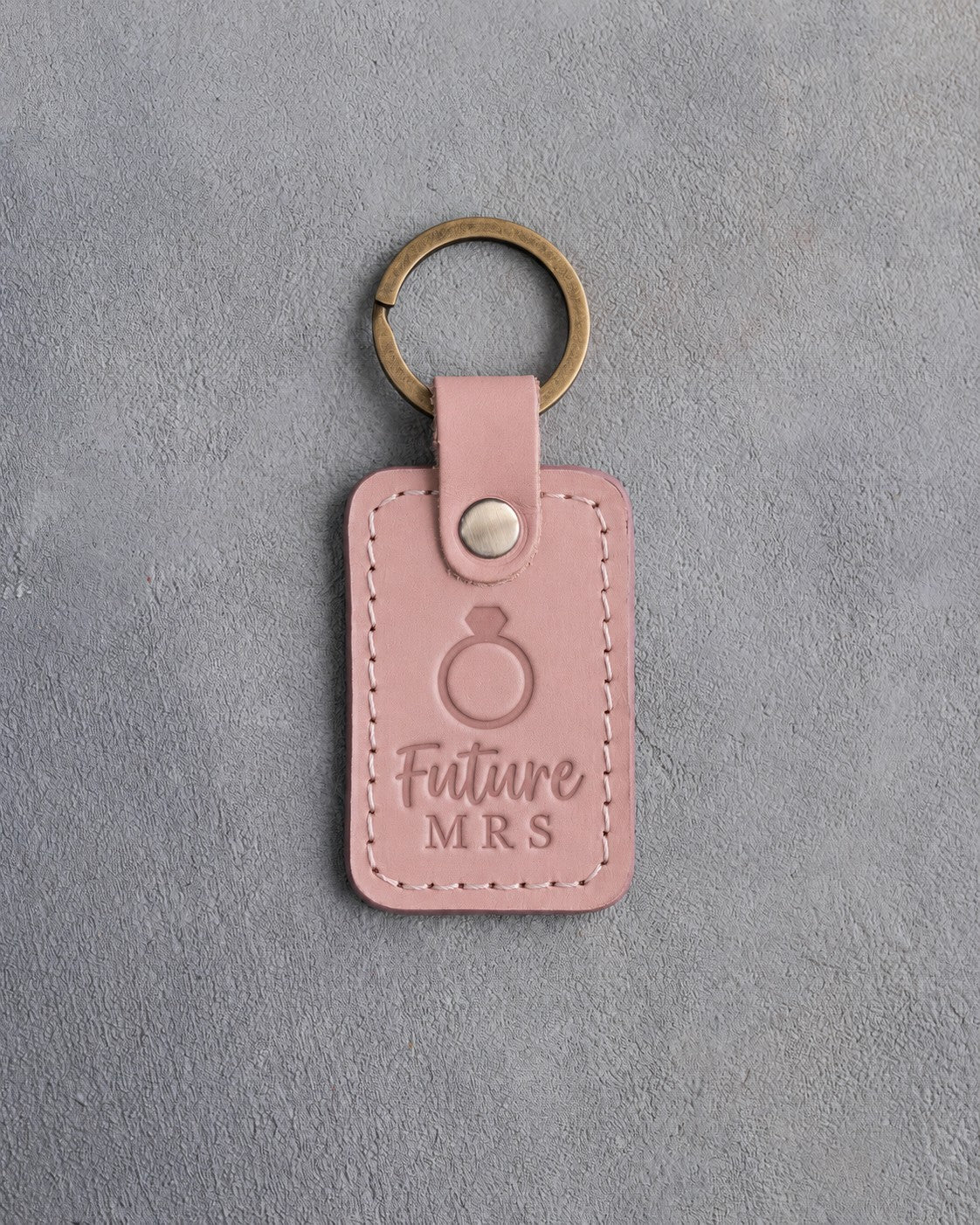 Blush pink leather keychain debossed with a solitaire engagement ring above the words Future MRS, on gray concrete
