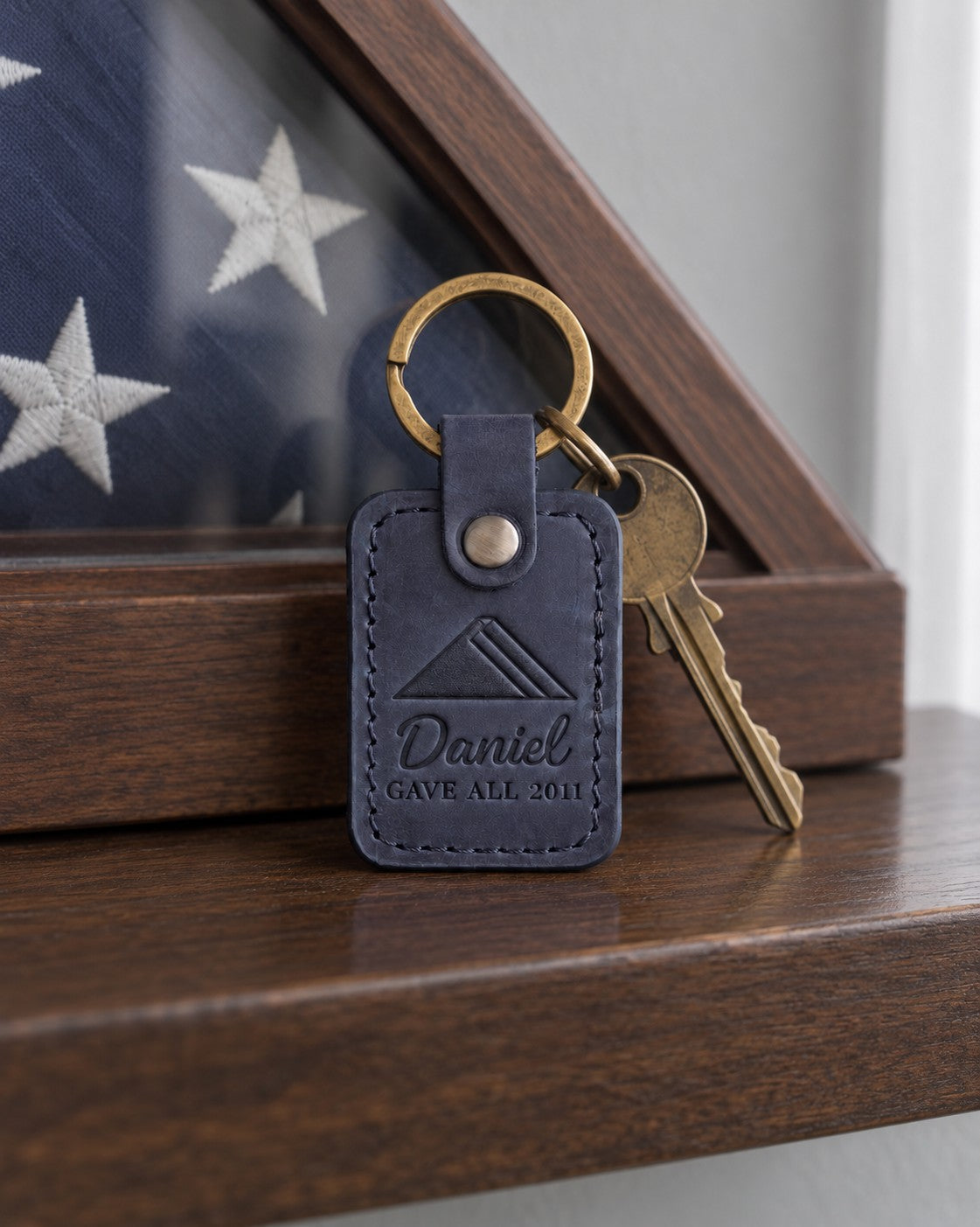 Navy Daniel Gave All 2011 keychain held in an open palm beside a folded flag on a wooden table