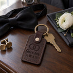 Gave her AWAY keychain in dark brown leather on a walnut hotel dresser beside cufflinks and a white boutonniere