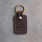 Dark espresso leather keychain debossed with two interlocked wedding rings above the words Gave her AWAY, on gray concrete