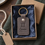 Gray Gemini keychain on a set of keys beside a wrapped birthday present on a sunny table
