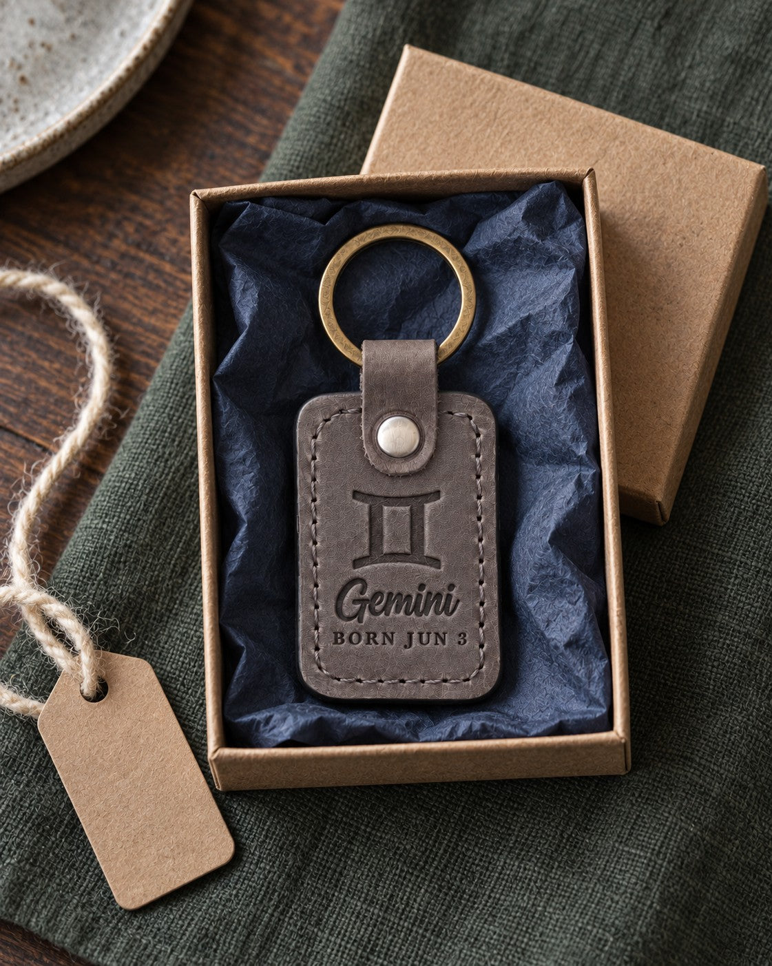 Gray Gemini keychain on a set of keys beside a wrapped birthday present on a sunny table