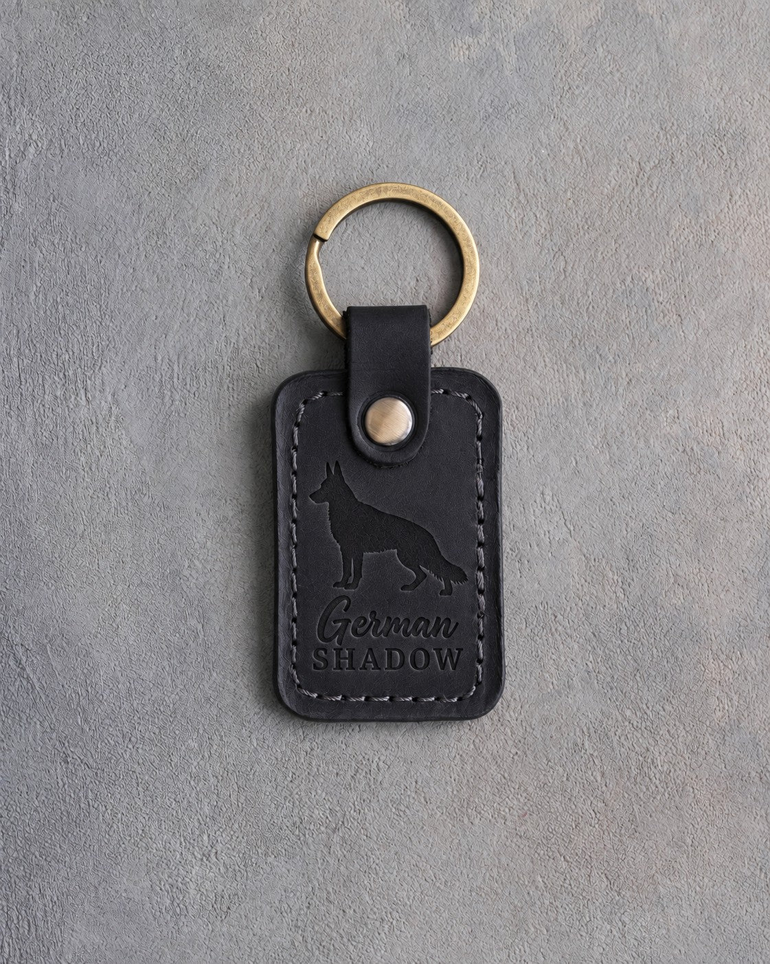 Black leather keychain debossed with a German Shepherd silhouette and the words German SHADOW, on gray concrete