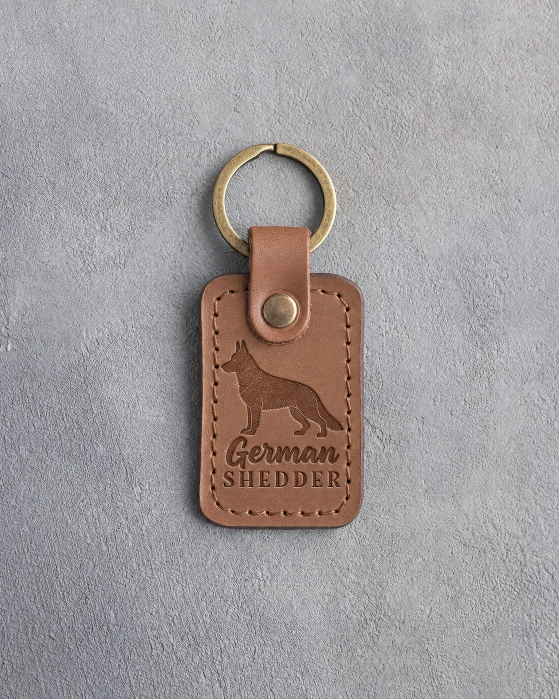Caramel leather keychain debossed with a German shepherd silhouette and the words German SHEDDER, on gray concrete