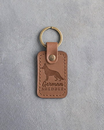 Caramel leather keychain debossed with a German shepherd silhouette and the words German SHEDDER, on gray concrete
