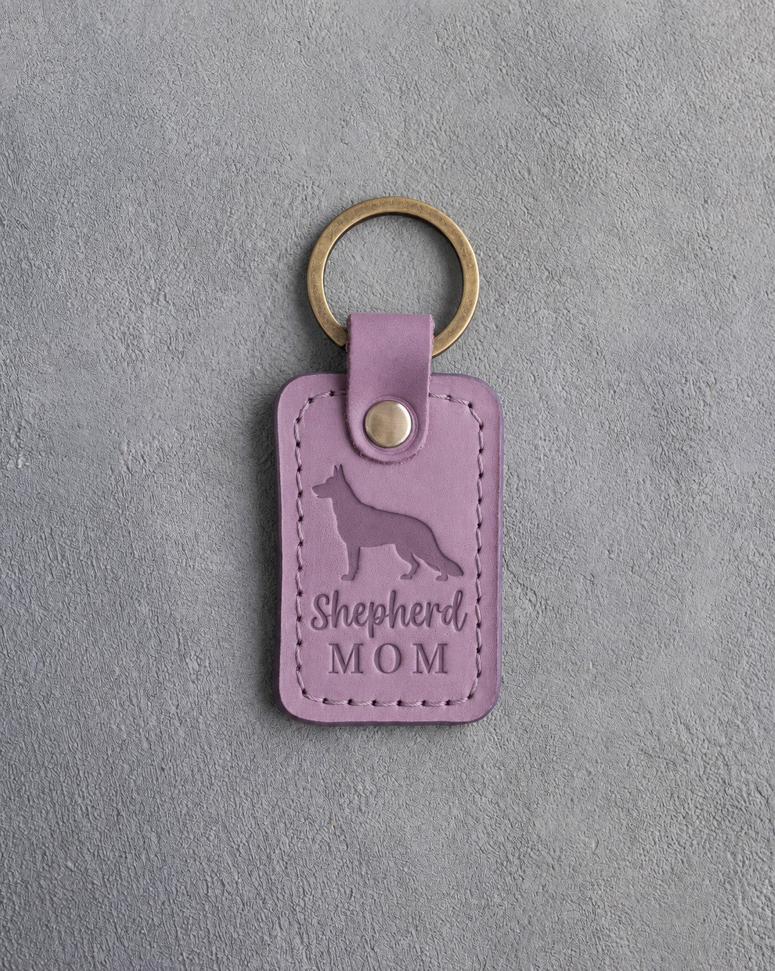 Lilac leather keychain debossed with a German Shepherd silhouette and the words Shepherd MOM, on gray concrete
