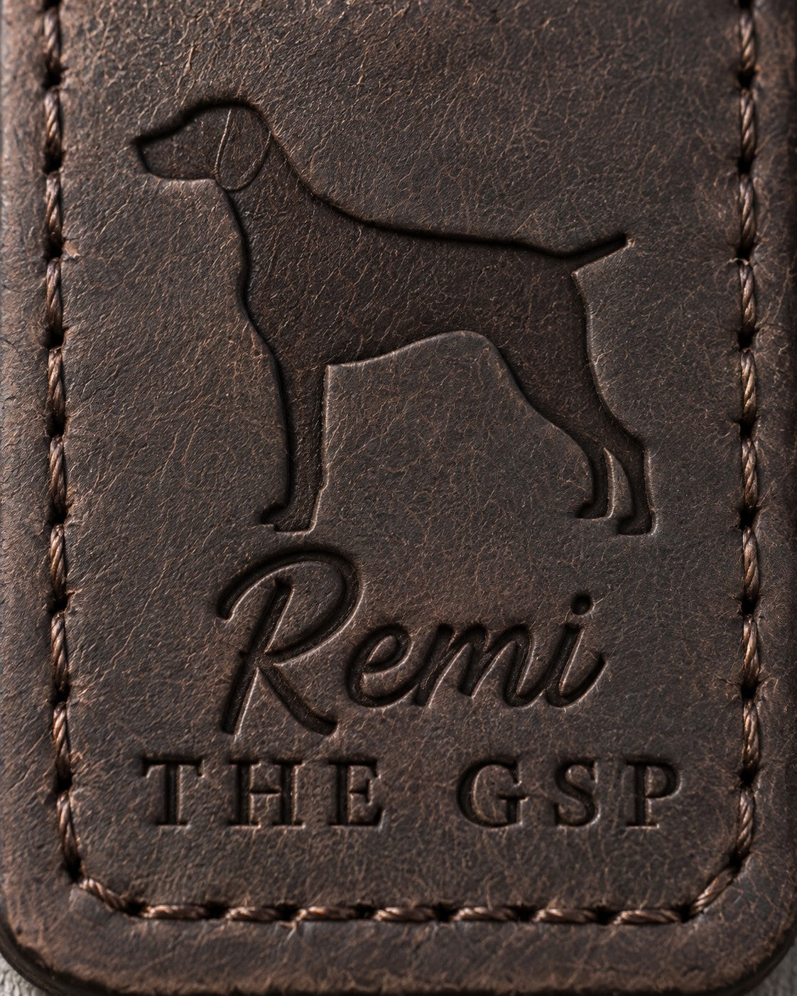 Close-up of Remi in brush script and THE GSP pressed into dark espresso full-grain leather beneath a German Shorthaired Pointer silhouette