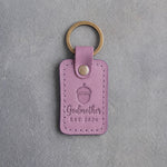 Lilac leather keychain debossed with a single acorn above Godmother and EST 2026