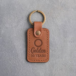 Caramel leather keychain debossed with a single wedding band above Golden and 50 YEARS, on gray concrete