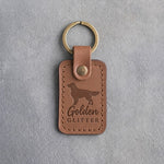Caramel leather keychain debossed with a golden retriever silhouette and the words Golden GLITTER, on gray concrete