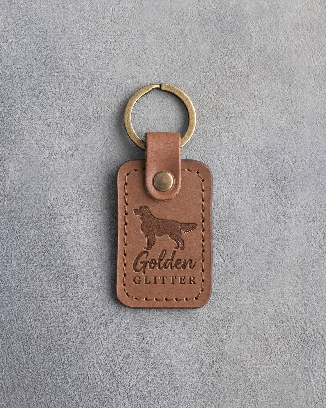 Caramel leather keychain debossed with a golden retriever silhouette and the words Golden GLITTER, on gray concrete