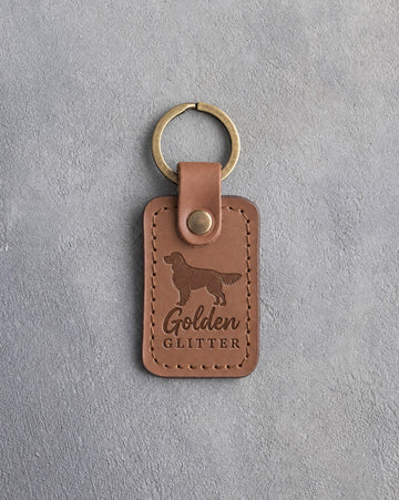 Caramel leather keychain debossed with a golden retriever silhouette and the words Golden GLITTER, on gray concrete