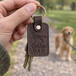 Golden Dad keychain in dark brown leather held up on a park path with a golden retriever on a leash behind