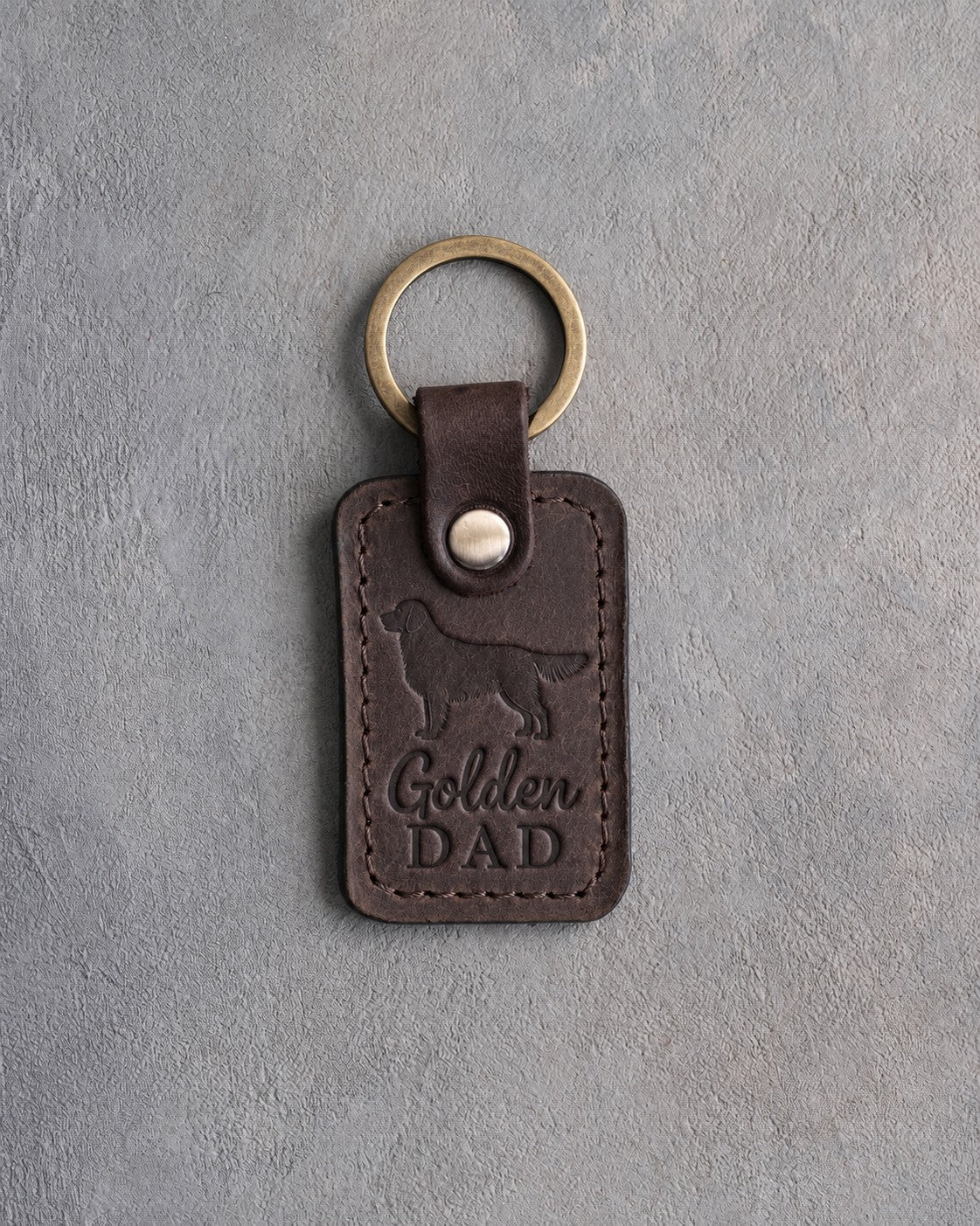 Dark espresso brown leather keychain debossed with a golden retriever silhouette and Golden DAD, on gray concrete