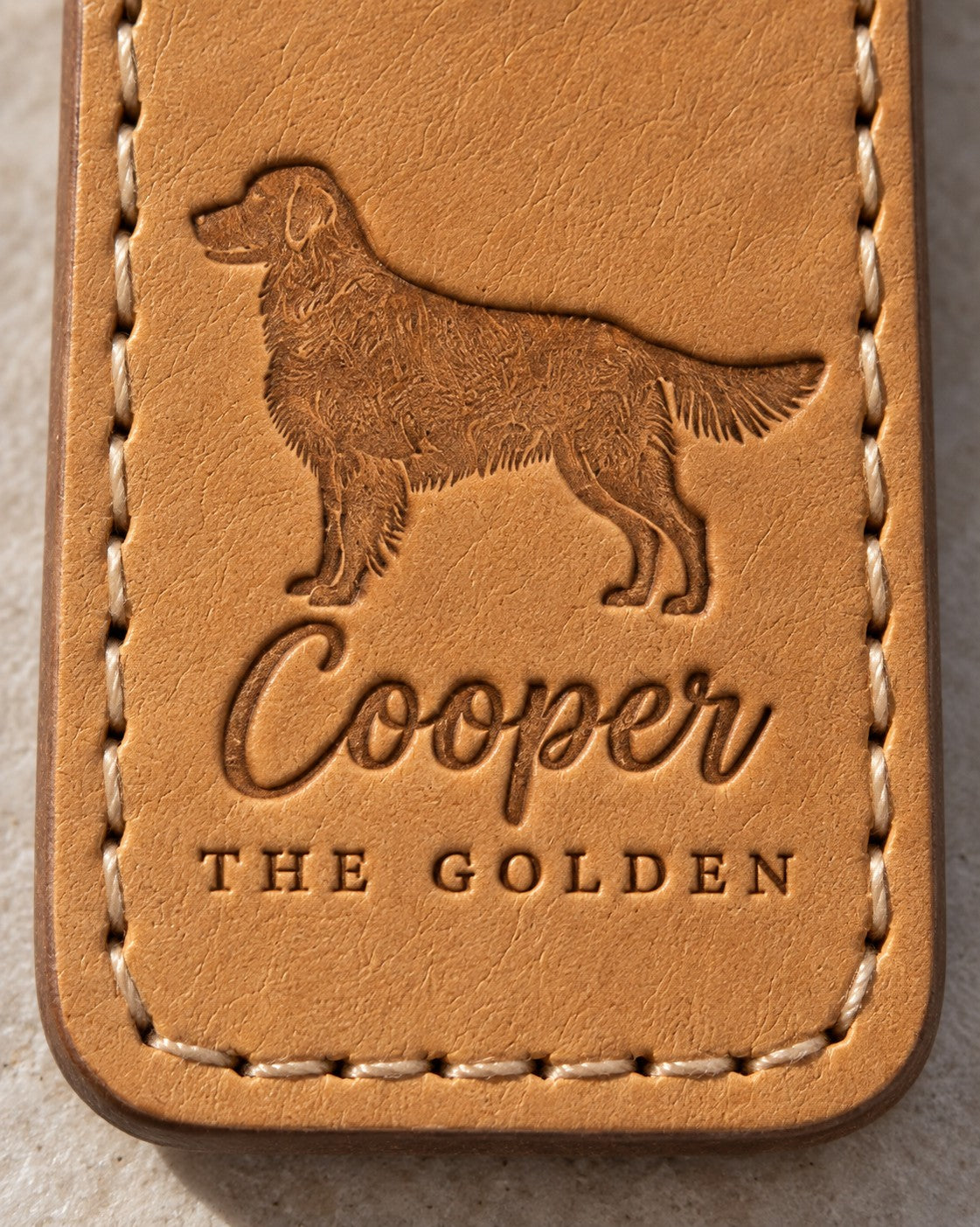 Close-up of Cooper in brush script and THE GOLDEN pressed into tan full-grain leather below a feathered golden retriever
