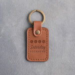 Caramel leather keychain debossed with four golf balls in a row above Saturday FOURSOME, on gray plaster