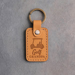 Golden tan leather keychain debossed with a golf cart above the words Golf GRANDPA, on gray plaster