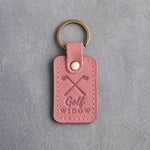 Rose pink leather keychain debossed with crossed golf irons above the words Golf WIDOW, on gray plaster