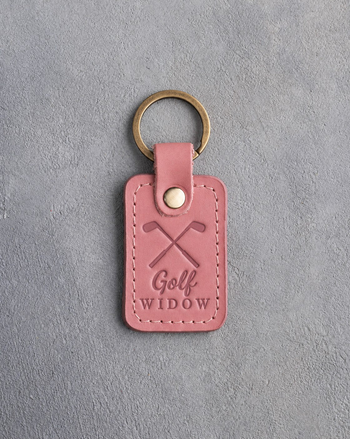 Rose pink leather keychain debossed with crossed golf irons above the words Golf WIDOW, on gray plaster