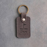 Country gray leather keychain debossed with a golf pin flag above the name Dave and ELM CREEK GC, on gray plaster