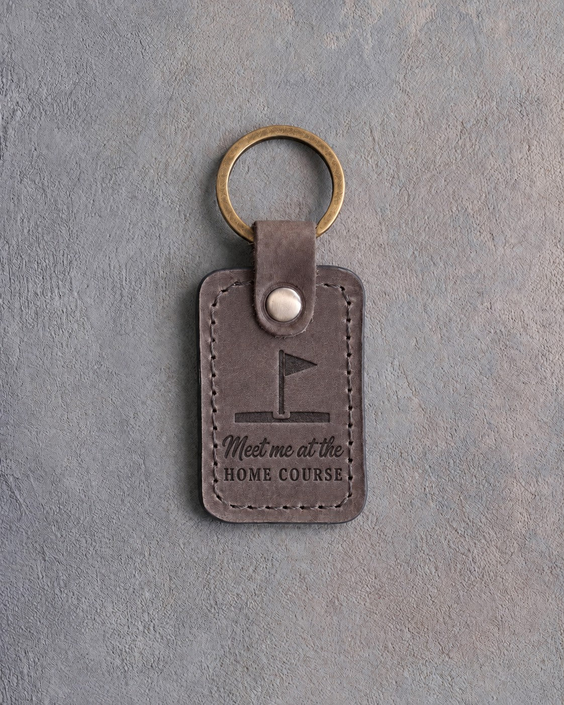 Country gray leather keychain debossed with a golf pin flag above the words Meet me at the and HOME COURSE, on gray concrete
