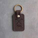 Dark espresso leather keychain debossed with crossed golf irons above the name Mike and SINCE 1998, on gray plaster