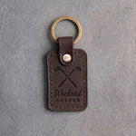 Dark espresso leather keychain debossed with crossed golf irons above the words Weekend and GOLFER, on gray concrete