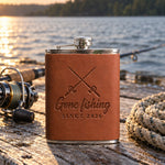 Arizona Gone fishing SINCE 2026 hip flask in full-grain leather on sun-bleached dock boards beside a spinning rod in low evening sun