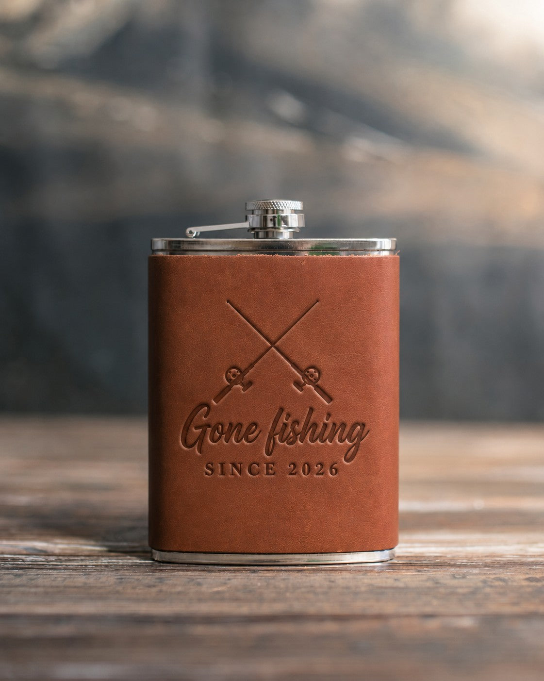 Arizona leather-wrapped hip flask debossed with crossed fishing rods above the words Gone fishing and SINCE 2026, on a wooden table