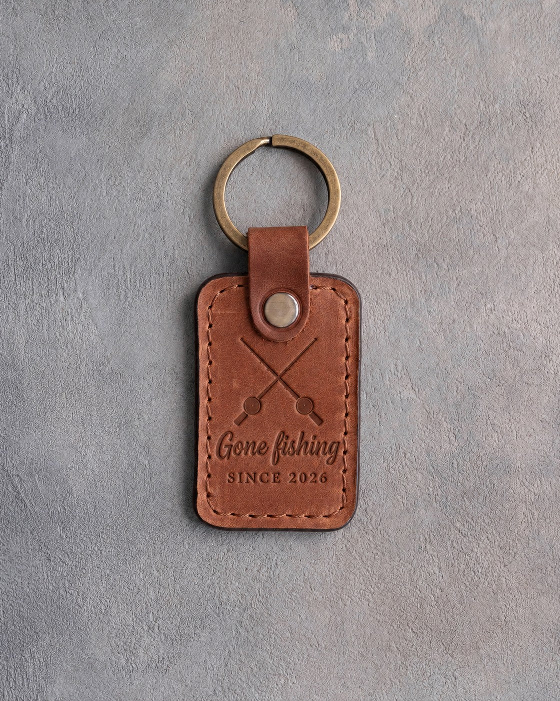 Arizona leather keychain debossed with crossed fishing rods above the words Gone fishing and SINCE 2026, on gray plaster