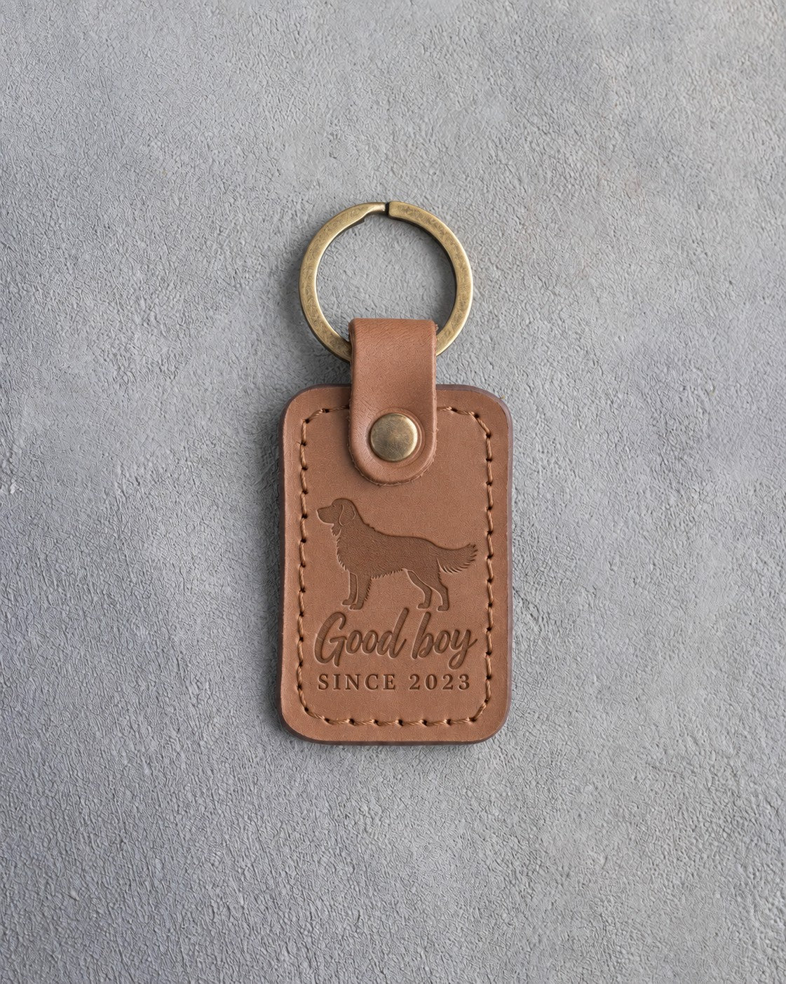 Caramel leather keychain debossed with a golden retriever and the words Good boy SINCE 2023, on gray concrete