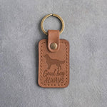 Caramel leather keychain debossed with a golden retriever and the words Good boy ALWAYS, on gray concrete
