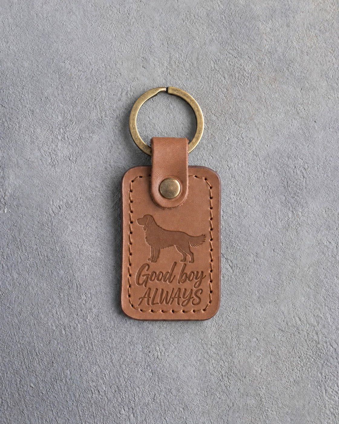 Caramel leather keychain debossed with a golden retriever and the words Good boy ALWAYS, on gray concrete