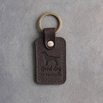 Dark espresso leather keychain debossed with a Labrador and the words Good dog IN TRAINING, on gray concrete