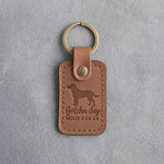 Caramel leather keychain debossed with a mixed breed dog above Gotcha day and MILO 3·14·24, on gray concrete