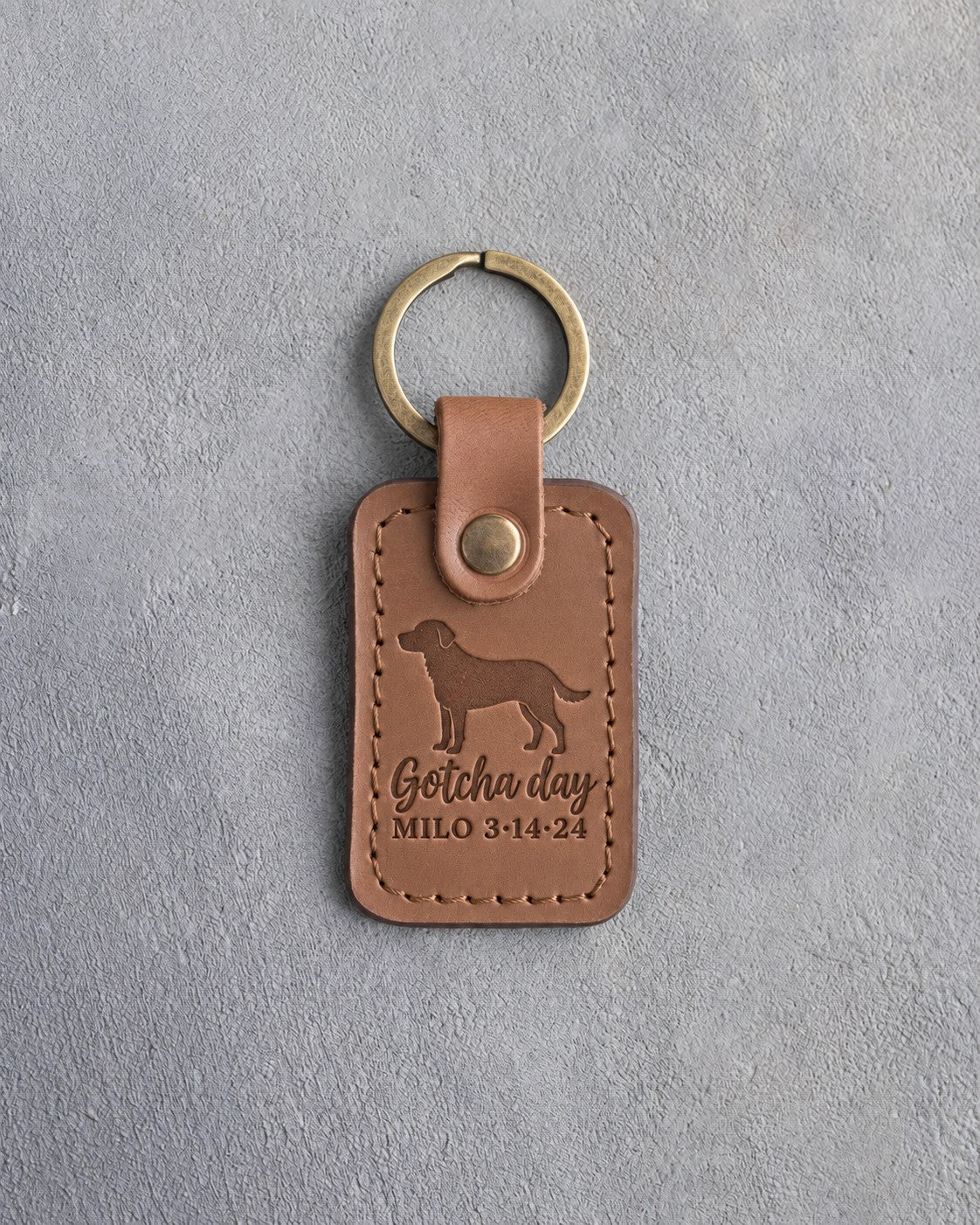 Caramel leather keychain debossed with a mixed breed dog above Gotcha day and MILO 3·14·24, on gray concrete