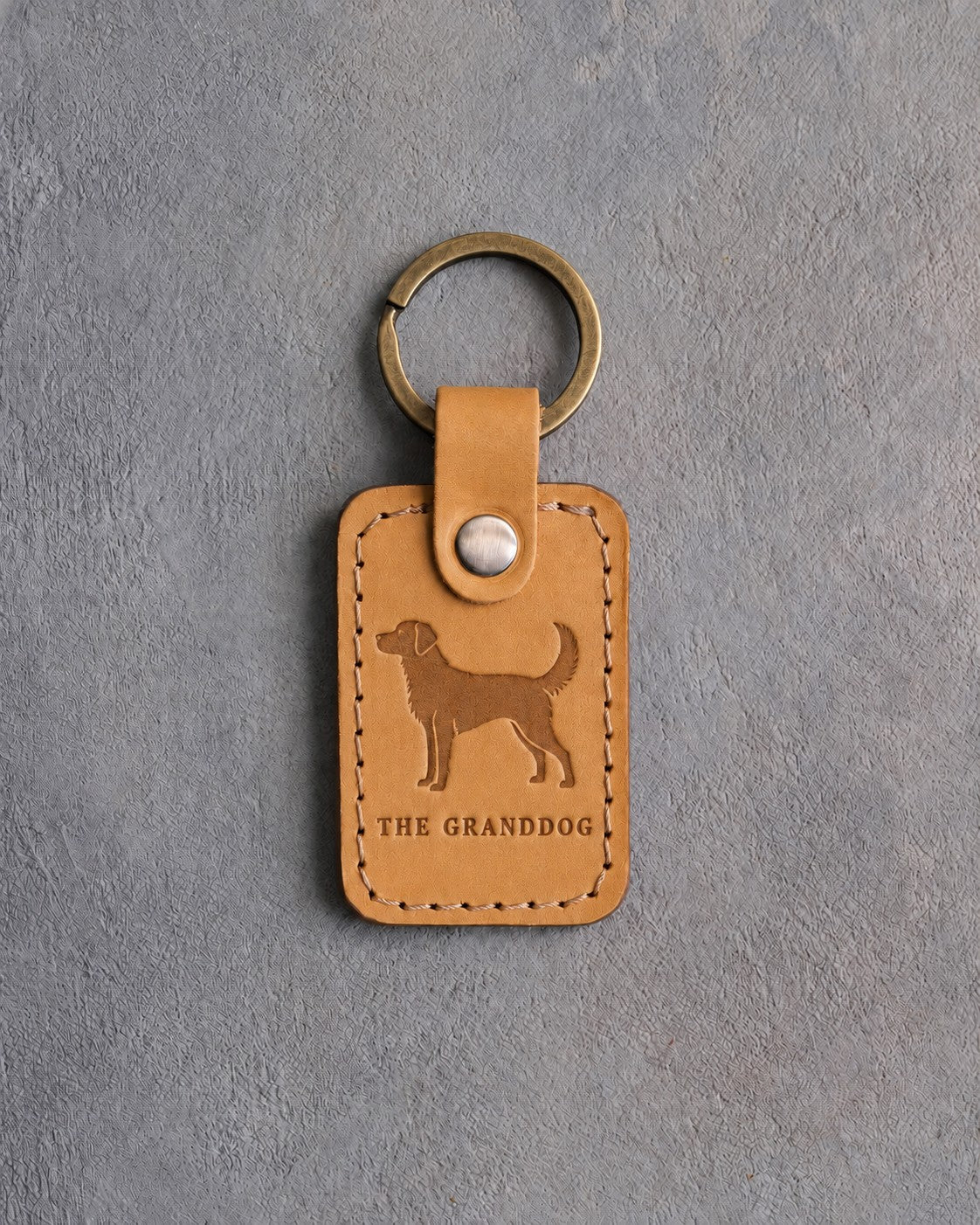Indian Summer tan leather keychain debossed with an alert dog above THE GRANDDOG, on gray concrete