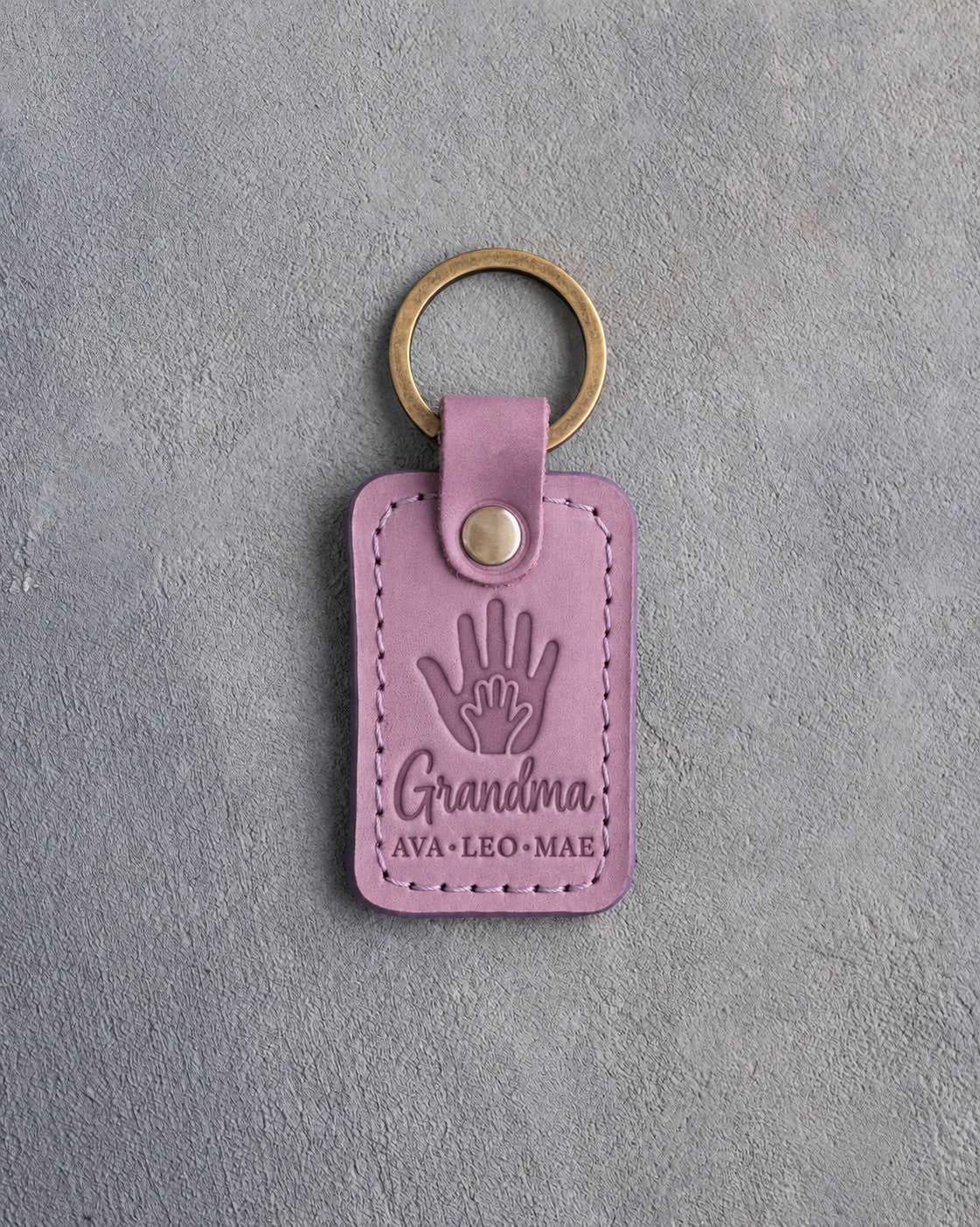 Lilac leather keychain debossed with a small hand inside a large hand above Grandma and AVA·LEO·MAE
