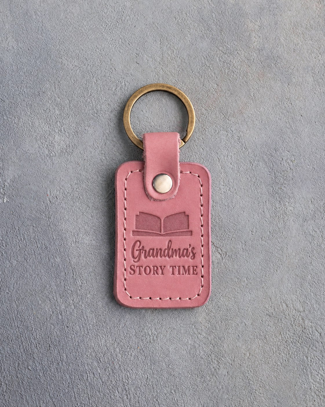 Parisian Blossom pink leather keychain debossed with an open book above Grandma's and STORY TIME, on gray concrete